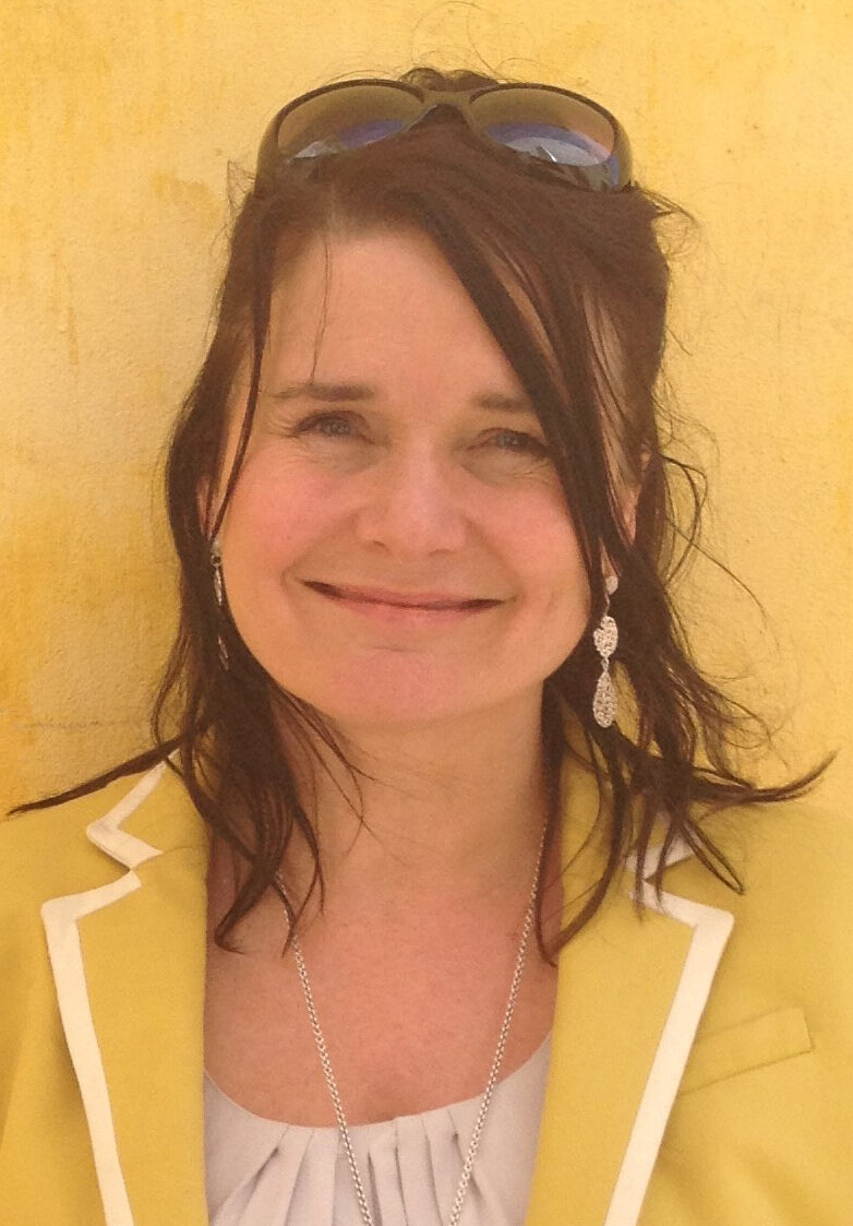 woman wearing yellow jacket and white top in front of a yellow wall