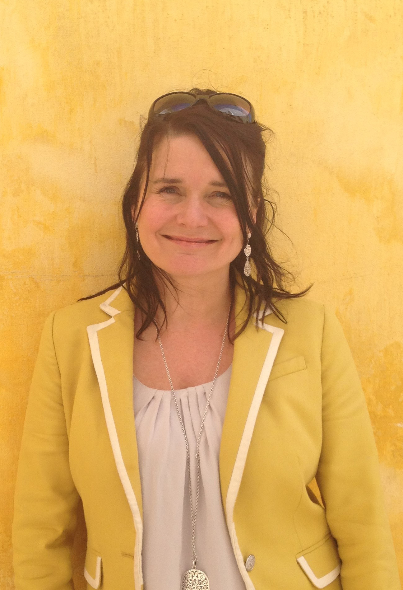 woman wearing yellow jacket and white top in front of a yellow wall