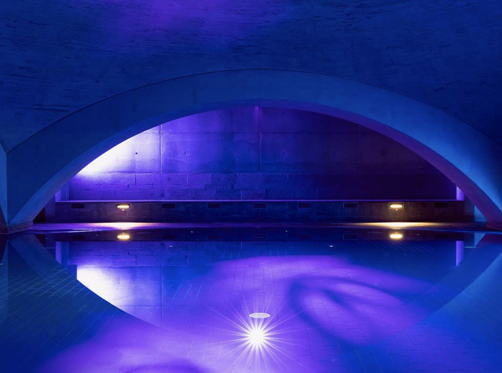 Picture of a subterranean pool in purple light with an arch shape over the top
