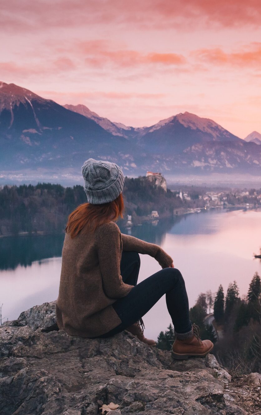 Picture of a woman in hiking gear sitting down to enjoy a dramatic sunset over the surrounding mountains