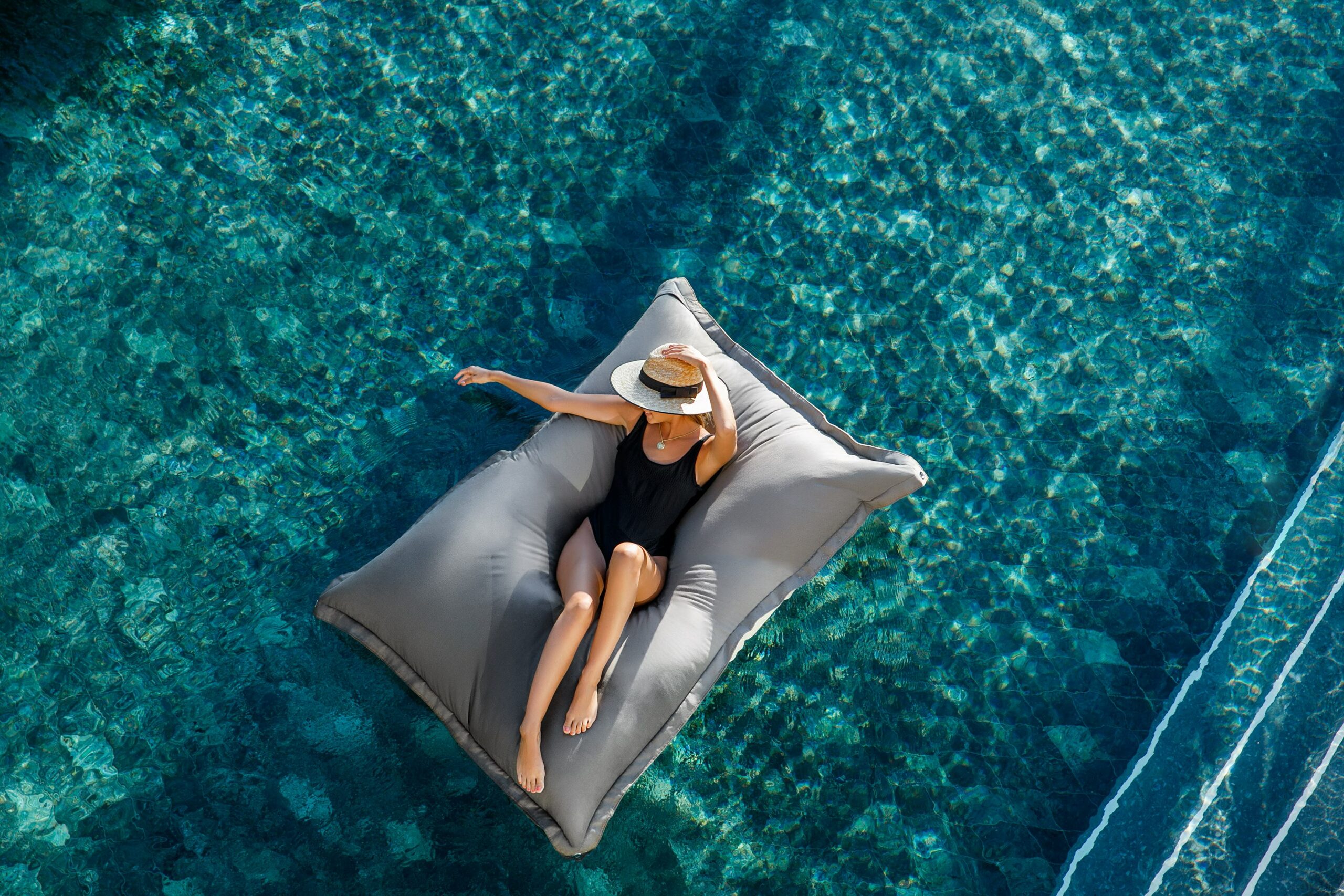 Aerial shot of a woman in a hat floating on an inflatable in a swimming pool