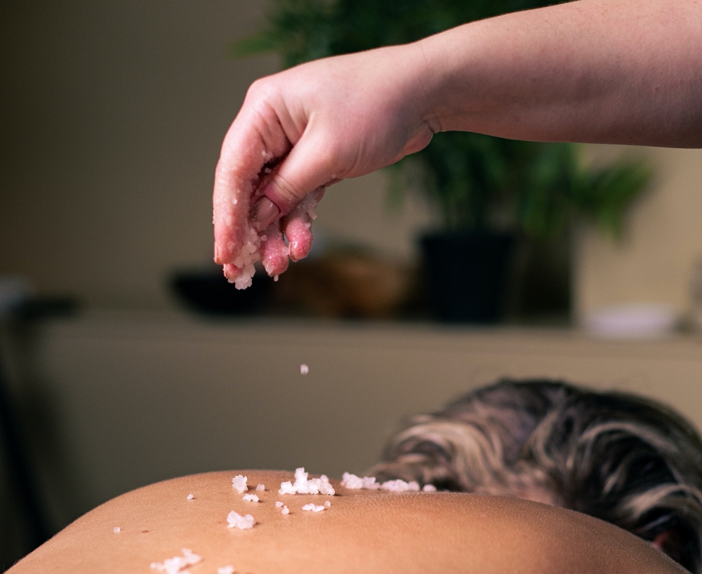A spa therapist's hand sprinkling salt on a guest's back during a treatment