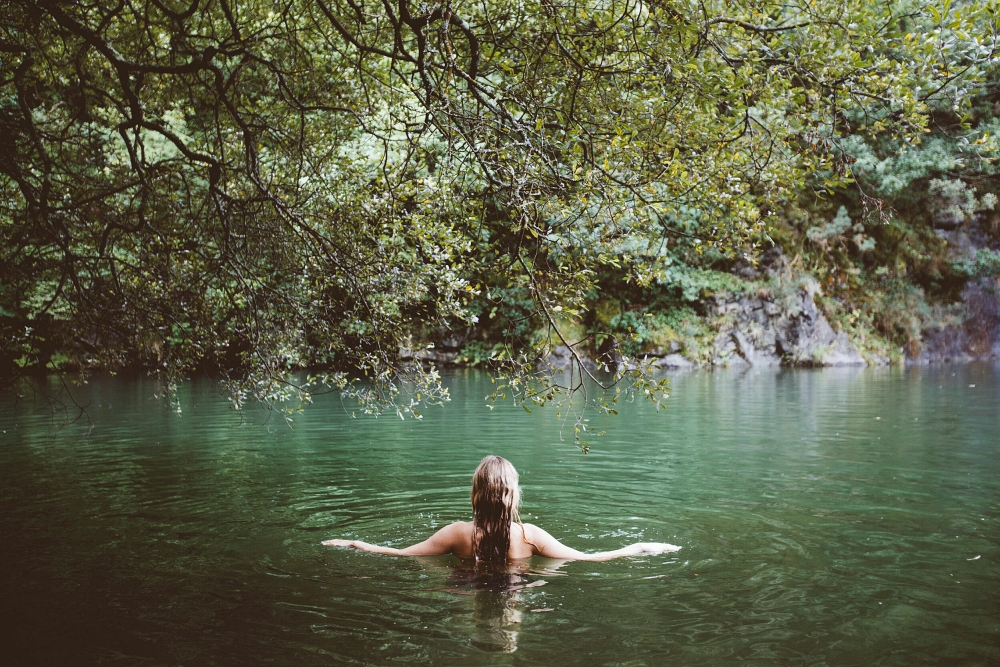 A woman in a green lake in front of trees