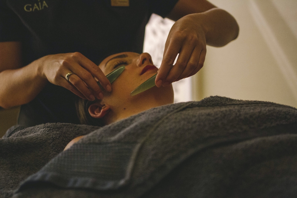 A spa therapist delivering a facial treatment to the a woman on a treatment bed