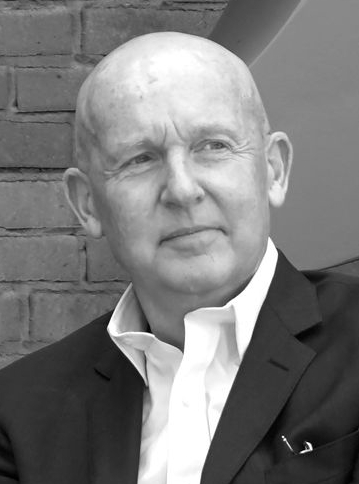 A black and white headshot of a bald man in front of a wall