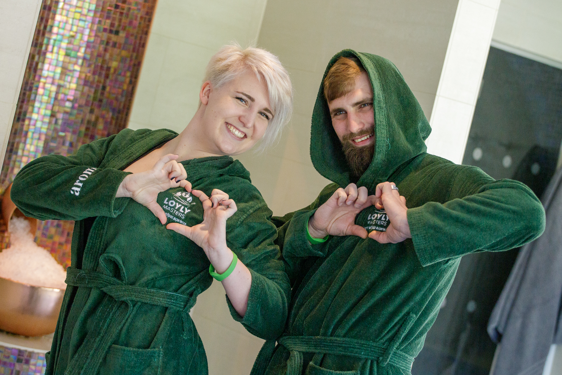 woman and man in green robes make heart shaped hands