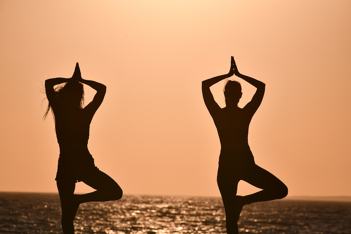 two people doing yoga on a beach at sunset