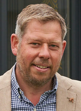 A man in a beige jacket and navy trousers