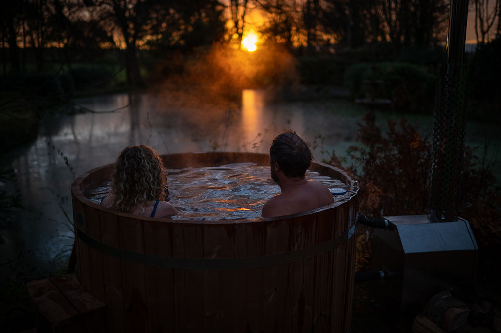 Couple sat in outdoor hot tub at sunset