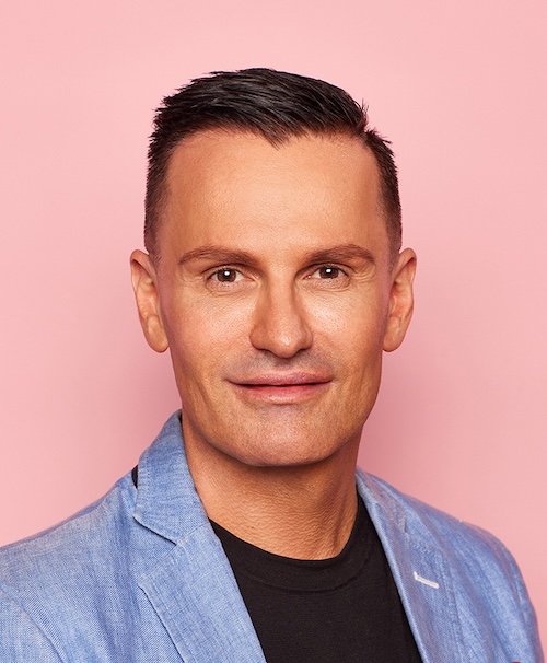 Portrait photo of man in blue jacket against pink background