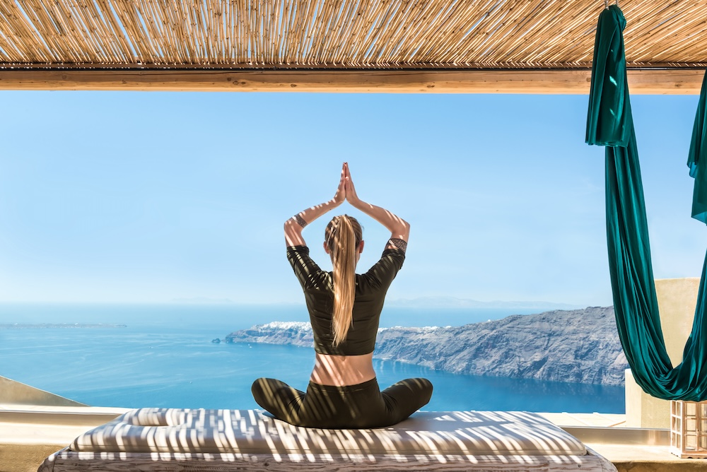 Woman sat in yoga pose overlooking bright blue ocean