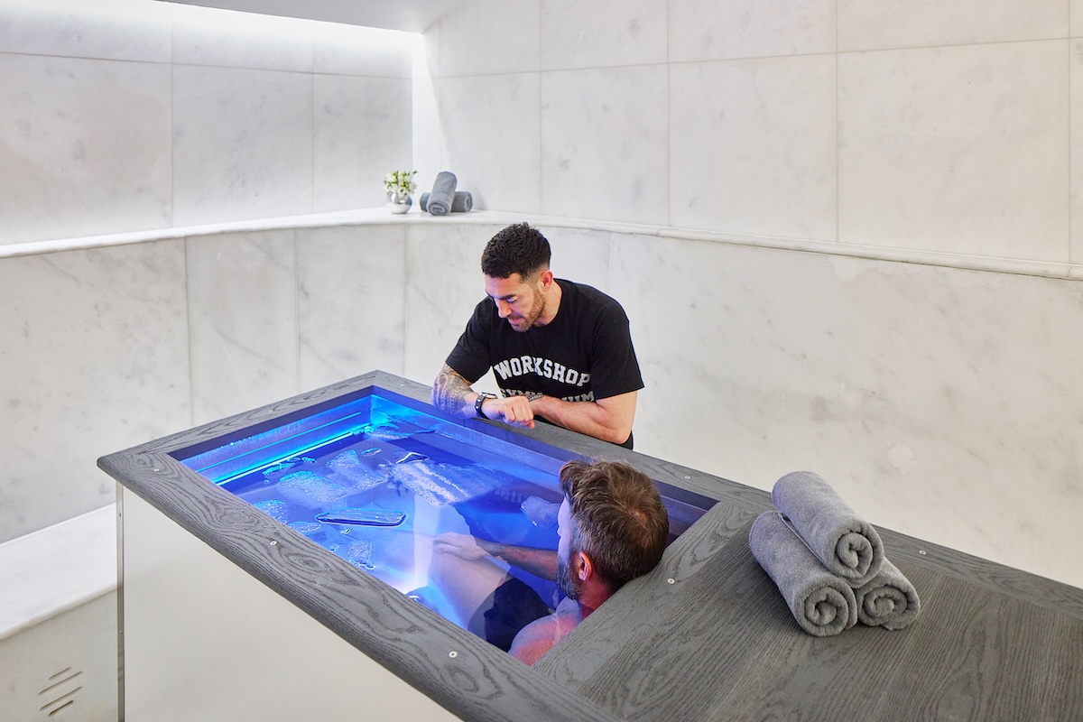 Man in ice bath with trainer stood at the side of the bath