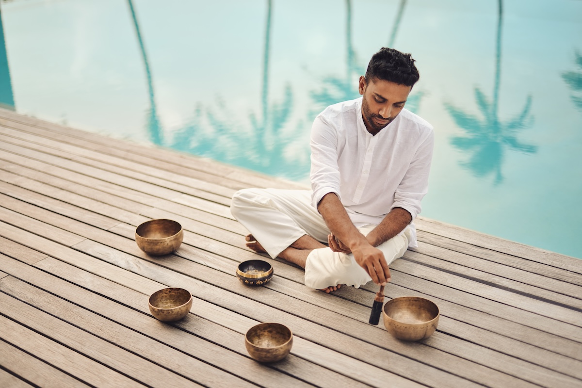 Man sat crossed legged using singing bowls