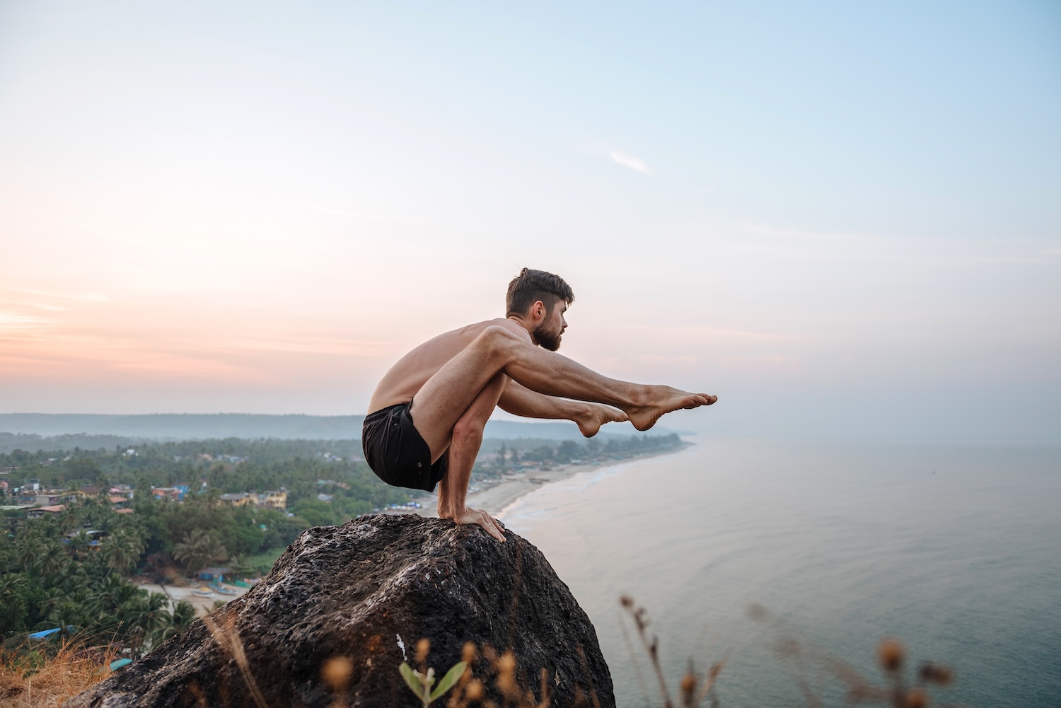 Healthy man practicing yoga under the beach at sunset.