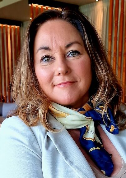 Woman in blue jacket and neck scarf sitting on a chair