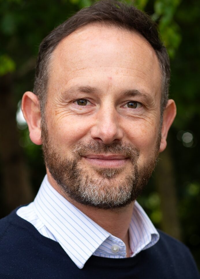 Headshot of man in navy jumper and white shirt