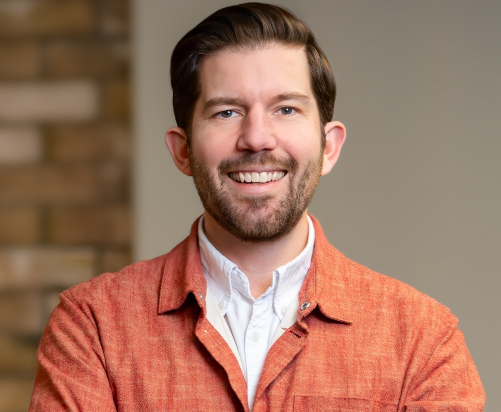 Headshot of smiling man with beard in orange shirt