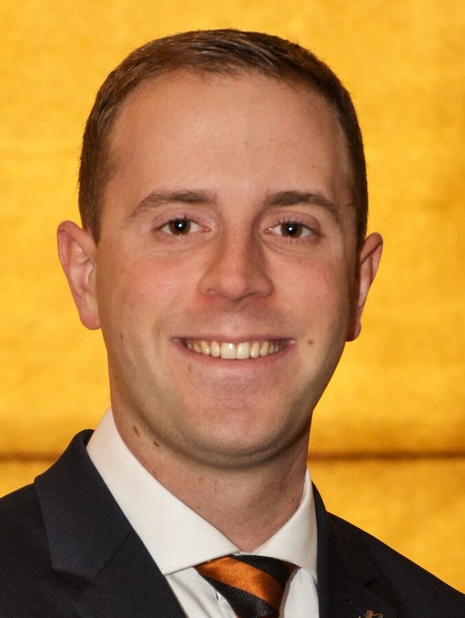 Smiling man in suit posing against mustard background