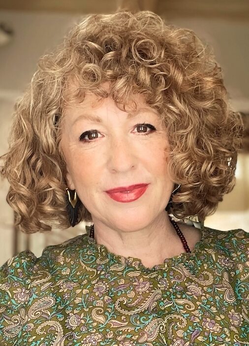 Woman in green top with short curly hair and red lipstick