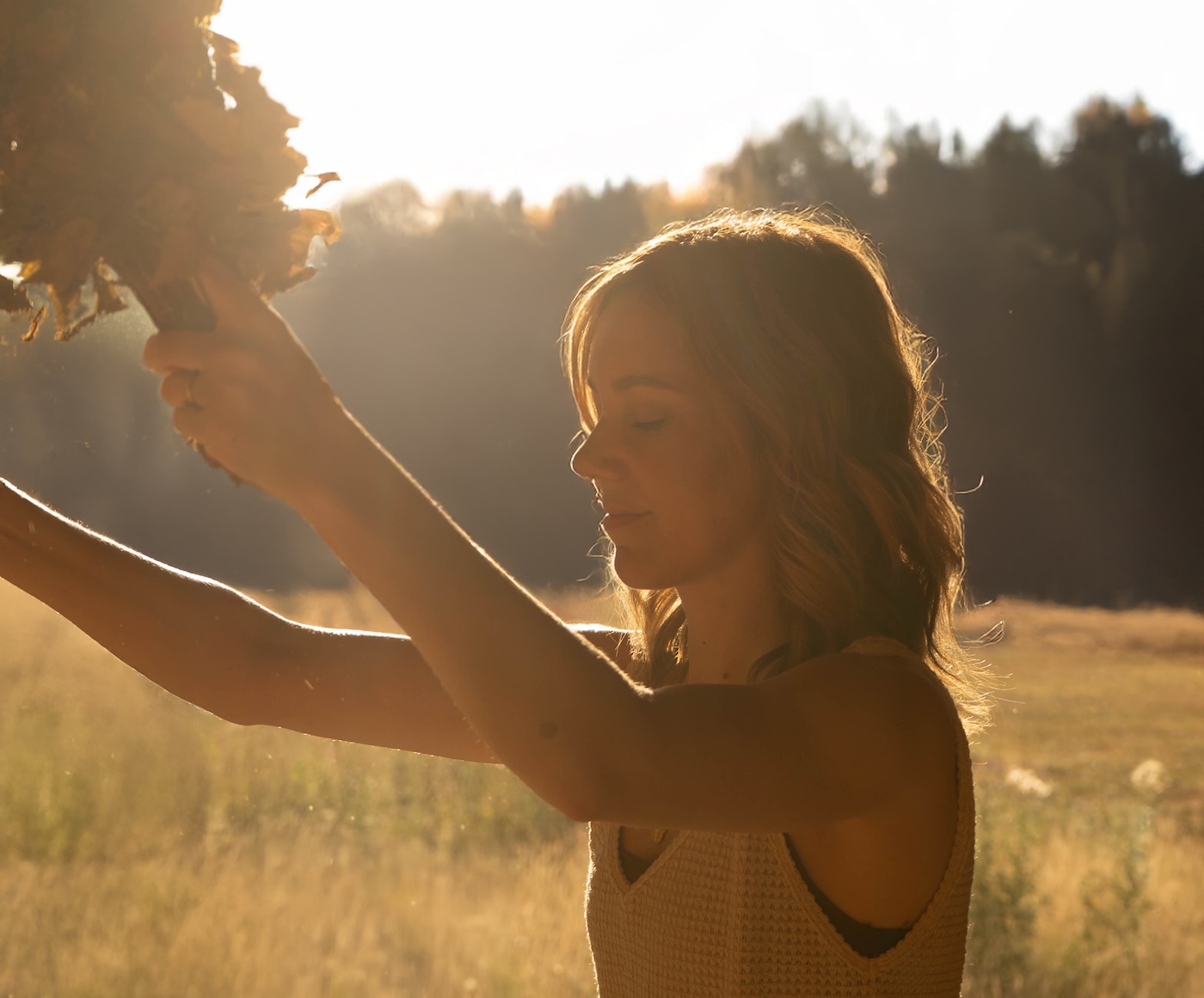 Woman holding onto leaves with sunset backdrop