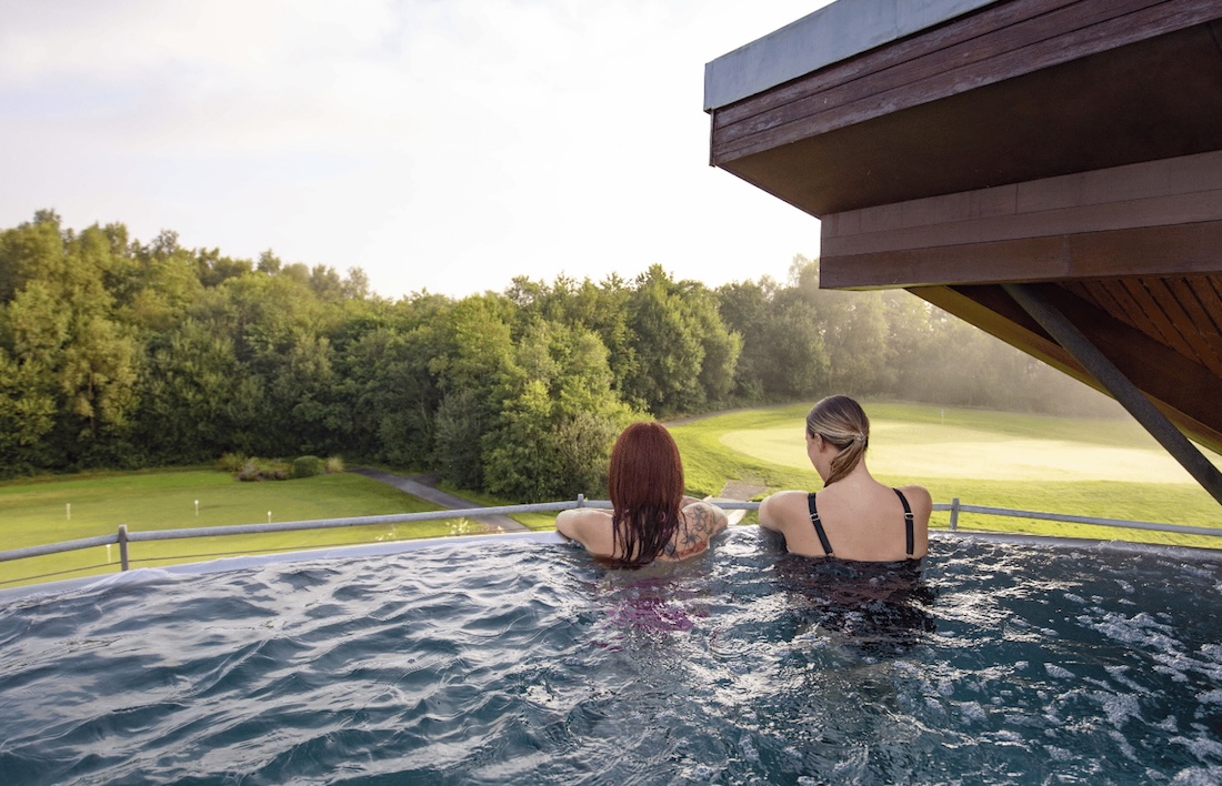 Two women sat in infinity pool overlooking Scottish countryside