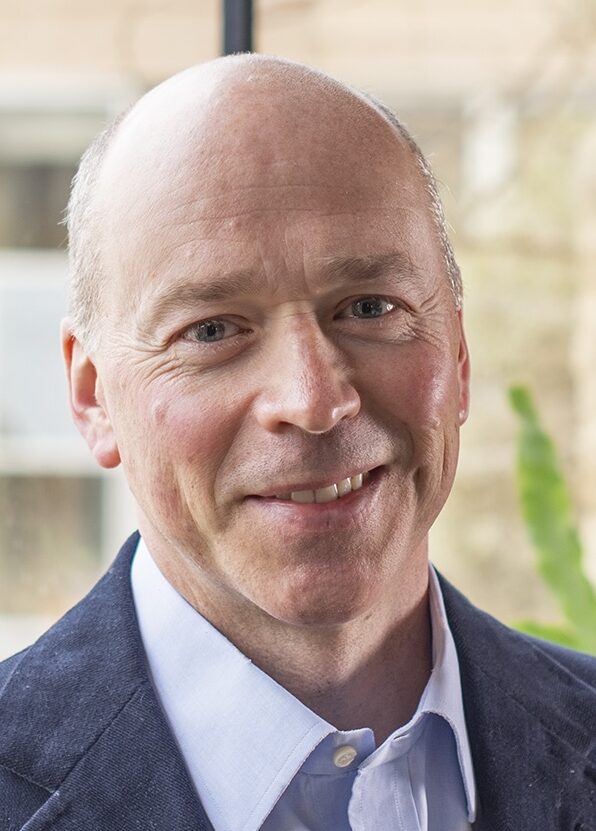 Headshot of smiling man with no hair wearing a suit
