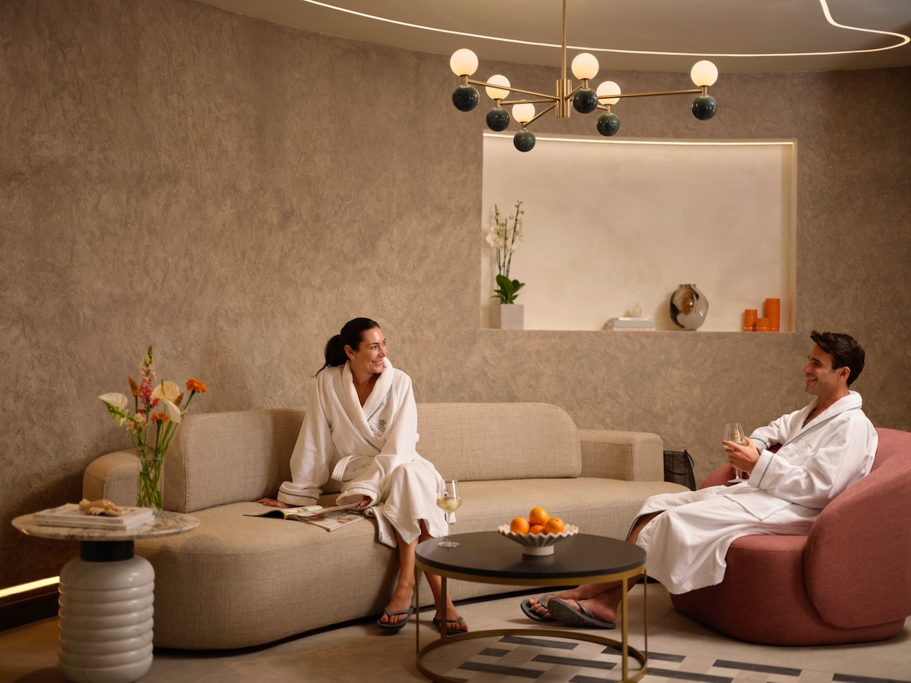 Woman and man in bathrobes sitting in a beige toned spa relaxation lounge