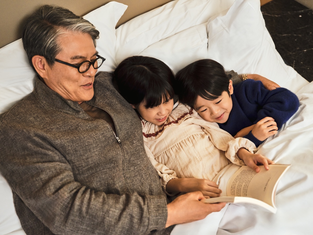 Grandfather reading to two small children all in the same bed