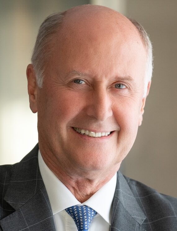 Headshot of smiling older man in grey suit and blue tie