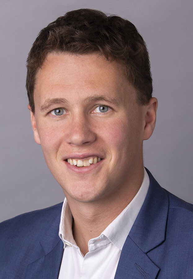 Posed headshot of young dark haired man in blue suit jacket