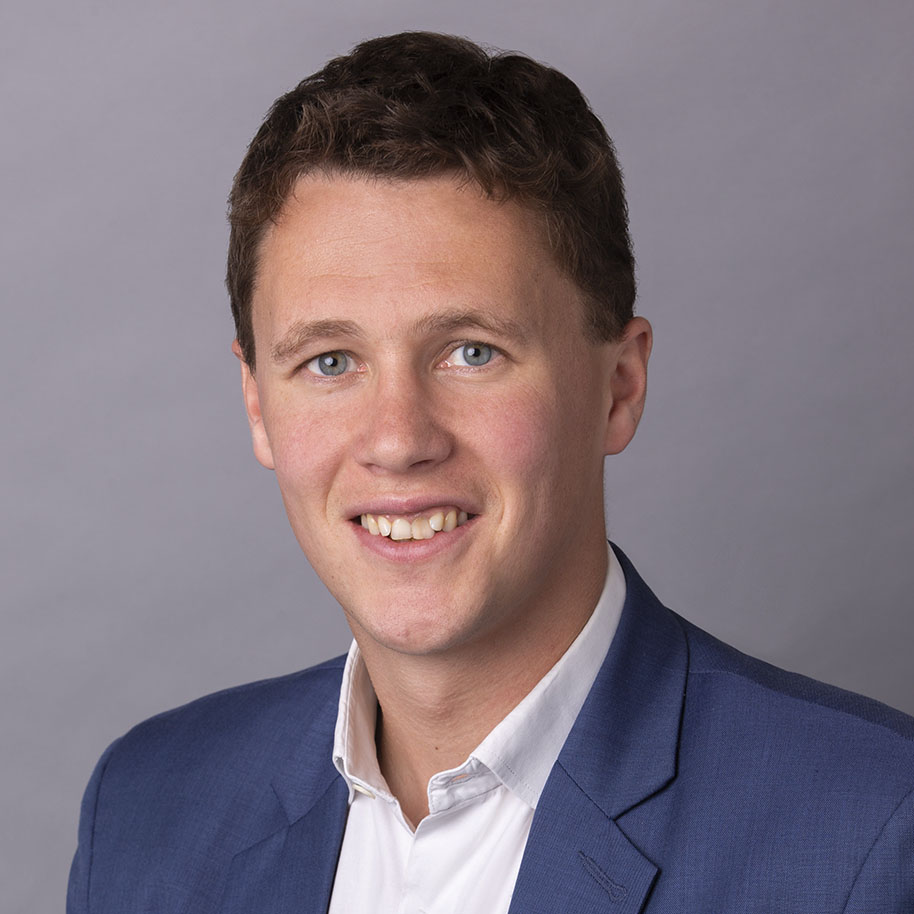Posed headshot of young dark haired man in blue suit jacket
