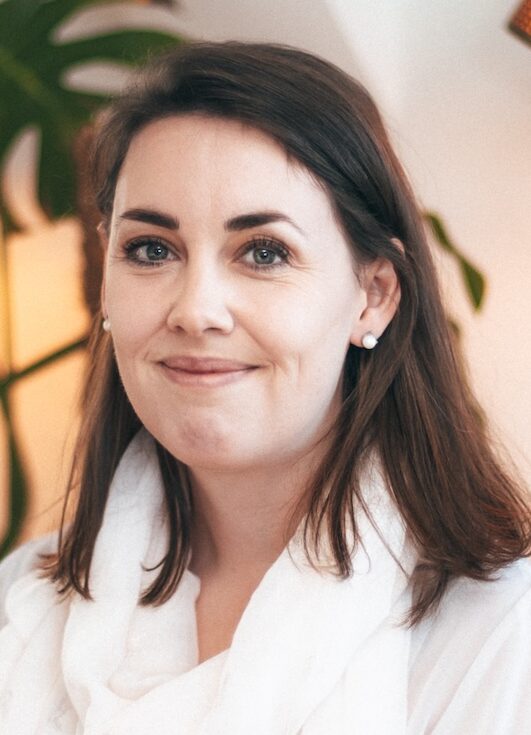 Smiling woman in white scarf, with shoulder length brown hair