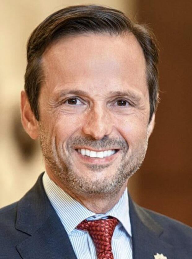 Head shot of dark haired man in grey suit with red tie