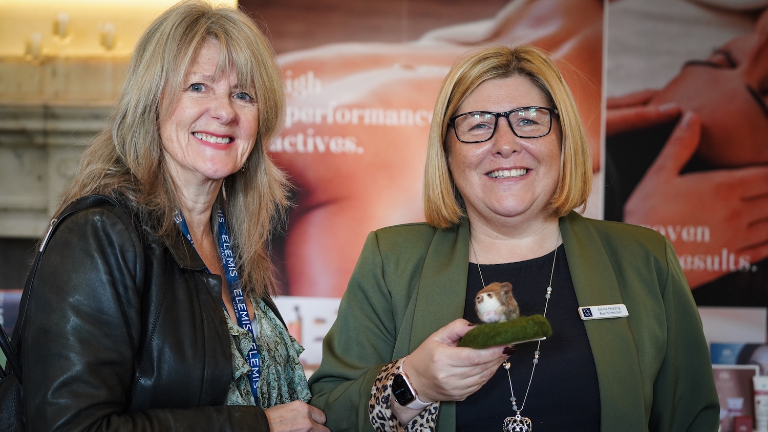 Two women posing for phot one holding a felt hedgehog