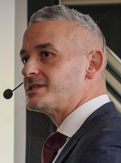 Man on stage giving a speech wearing grey suit