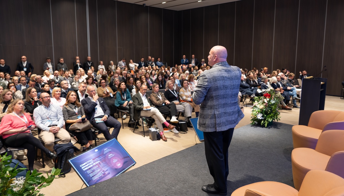 Man in tartan jacket addresses a roomful of people at a conference