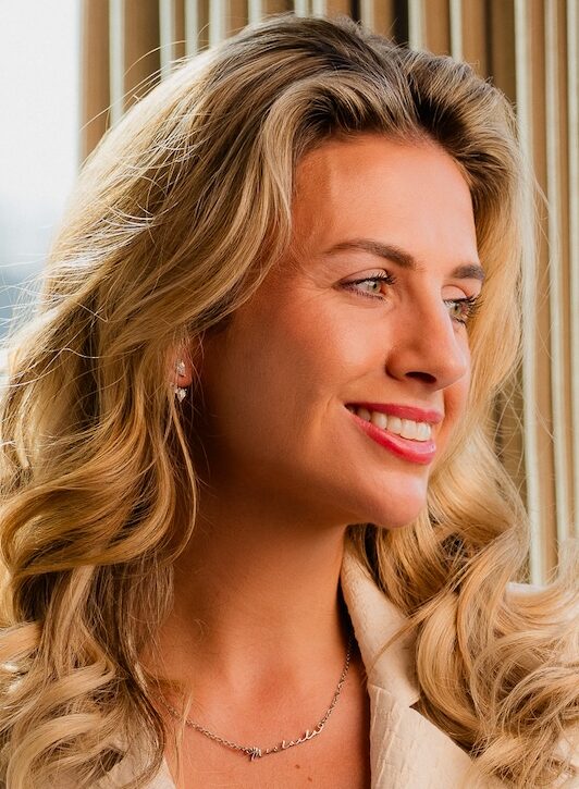Woman with long blonde curly hair wearing beige jacket