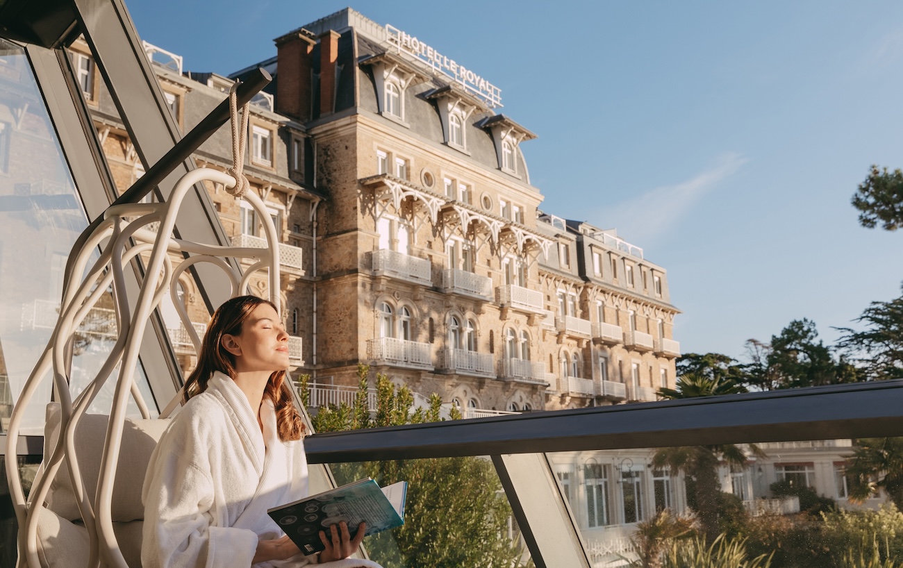 Woman sat on hotel balcony in bathrobe with book