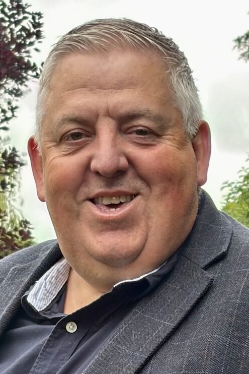 Older man in grey suit with pink handkerchief in pocket
