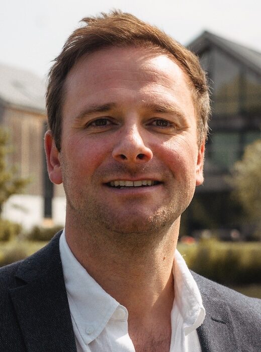 Smiling man in suit stood in front of lake