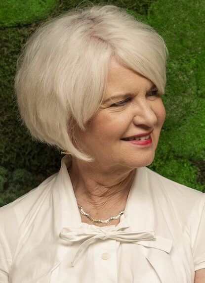 Woman in shite shirt with white heard leaning against a living wall